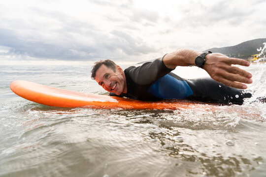 Middle aged sportive handsome man learning to surf, smiling in ocean water