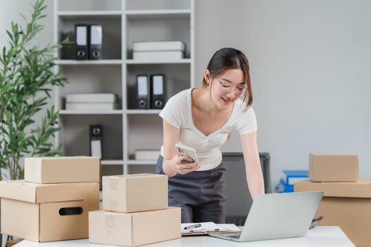 Small Business Owner at Work: A young woman, likely a small business owner, diligently manages her online orders and inventory, surrounded by shipping boxes and a laptop, in a home office setup.