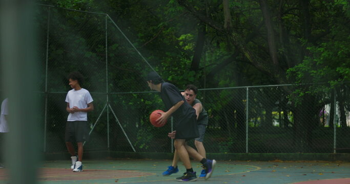 African American and Hispanic friends playing basketball on outdoor city court, teamwork and movement in friendly game showing energy, focus, and urban camaraderie