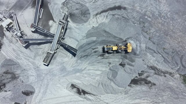 A large vehicle is moving and processing granite materials at a quarry location. Conveyor systems are visible in the background, transporting crushed stone.