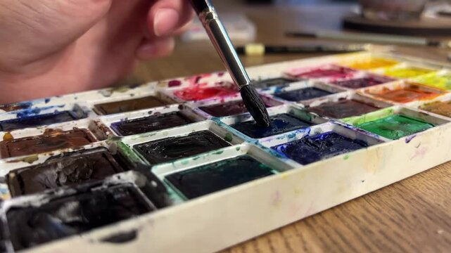 Watercolor paint set with brush picking up paint close up, watercolor painting