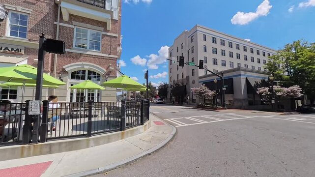 Sunny day street view of historic downtown Gainesville, Georgia. Charming brick buildings, blooming trees, wide intersection with traffic lights, and classic Southern small-town architecture