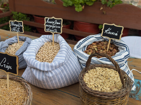 Traditional Greek legumes and grains in fabric sacks and wicker baskets with labels for wheat, manarolia peas, apostoliano white-eyed beans, fava broad beans and zea emmer wheat.
