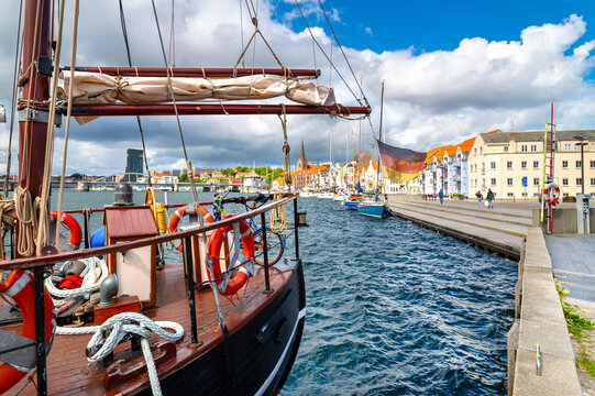 Historic sailing vessel with German flag in the harbor of Sonderborg beneath a blue summer sky overlooking the waterfront promenade. Denmark