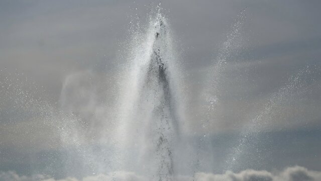 Large fountain spraying water high into cloudy sky on sunny day outdoors