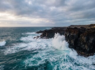 Obraz premium Aerial view of powerful ocean waves crashing against dark volcanic cliffs