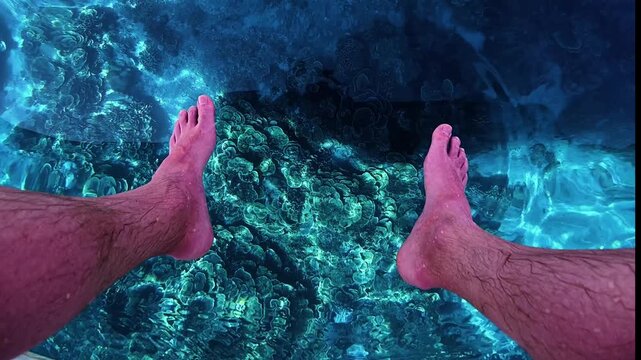 Feet dangle above crystal clear waters and Montipora coral reef near Gili Trawangan, Bali. Vibrant underwater life and turquoise sea create the perfect moment of relaxation and tropical escape.