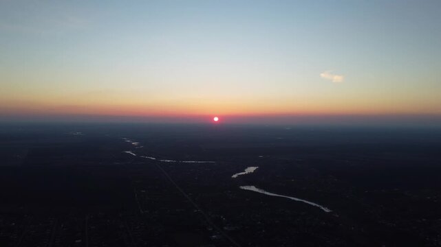 An expansive panoramic aerial shot captures the vibrant sunset over a sinuous river and urban area. The horizon is bathed in beautiful warm and cool tones.