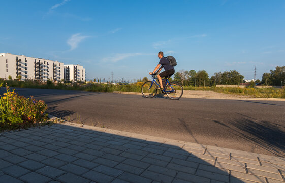 Side view of a man with a backpack riding a bicycle on a path near modern residential buildings