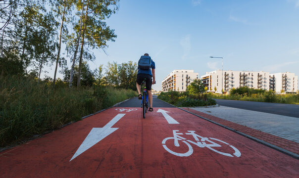 Low angle shot of a cyclist riding past a painted bicycle lane symbol on a red bike path