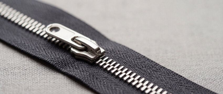 Close-up of metal zipper slider on black fabric showing teeth and textile texture