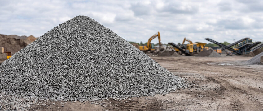 Large gravel pile at active construction site with excavators and heavy machinery in background