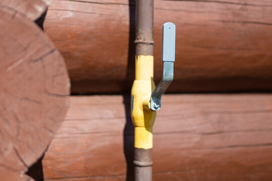 Outdoor pipe and faucet mounted on a wooden log wall, home utility detail, water supply, rustic construction, garden maintenance.
