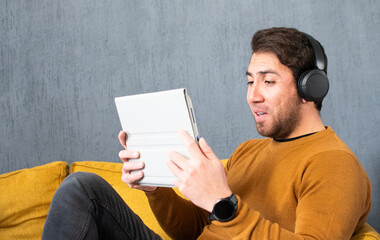 Focused man holding a tablet while wearing wireless headphones © Diego D