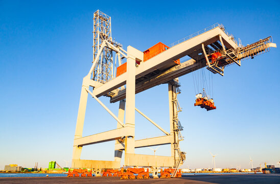 Large ship to shore gantry crane with twin lift spreader mechanism at a container terminal quayside against clear blue sky