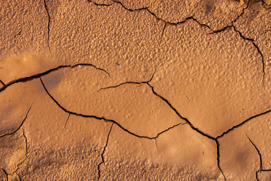 Deep cracks texture on parched dry orange clay ground, detailed arid soil surface pattern resulting from extreme heat and lack of water in a drought stricken landscape