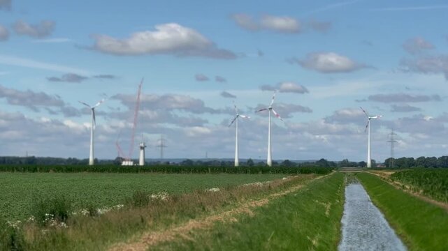Wind farm beside agricultural fields and drainage canal - Panoramic view of a wind farm beside cultivated farmland and a drainage canal under a bright summer sky. Renewable energy, sustainable land us