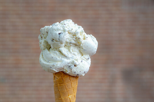 Selective focus of white chocolate chip (stracciatella gelato) flavor in crispy cone with blurred bricks wall as background, Refreshing and cool down after warm day in summer with soft ice cream.