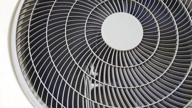 Slow motion close-up of rotating condenser fan blades inside a modern outdoor air conditioner unit. Industrial