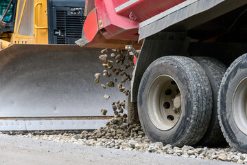 Close-up of a heavy dump truck unloading crushed stone or gravel in front of a bulldozer metal blade during road construction. © Alexander Korotkov