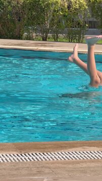 Funny young boy diving upside down in a blue resort swimming pool with only his feet sticking out of the water. The kid is having fun, catching positive vibes, and enjoying his active summer vacation 