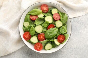 Naklejka premium Appetizing salad with spinach, tomatoes and cucumbers served on grey table, top view