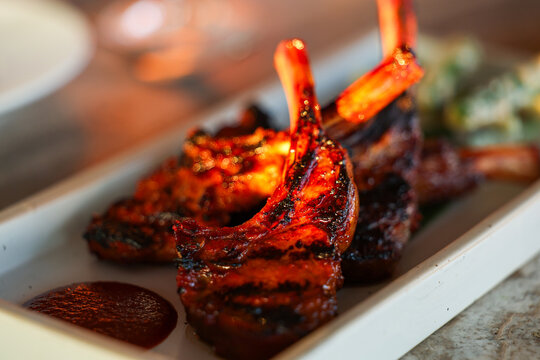 Grilled lamb chops glow in warm sunset light, highlighting charred edges and rich caramelization &mdash; a gourmet dish capturing the essence of Mediterranean dining and golden-hour culinary artistry.