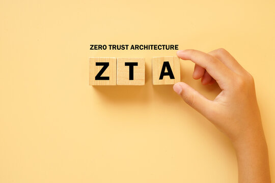 Hand arranging wooden letter blocks spelling ZTA with the words Zero Trust Architecture above on a bright background. Concept of cybersecurity, identity verification and secure network access.