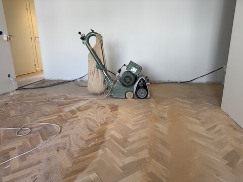 Floor sander in room with parquet flooring and dust