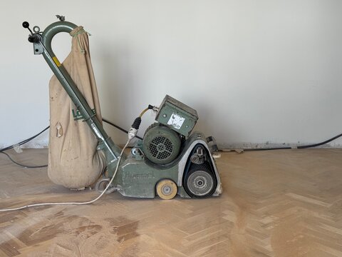 A floor sander machine with a dust bag sits on a wooden parquet floor on June 29, 2026 in Boulogne-Billancourt, France