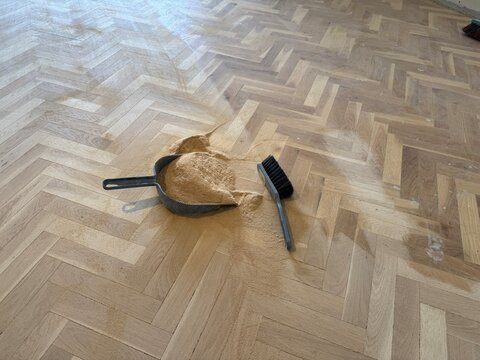 Dustpan and brush on sanded wooden parquet floor