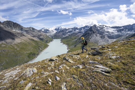 Mountaineer on the summit of Mont de la Blana, view of a blue mountain lake, Lac des Dix reservoir, behind mountain peak Mont Blanc de Cheilon with glacier, H&eacute;rm&eacute;nence, Valais Alps, Valais, Switzerland
