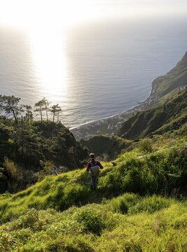Young man looking out to sea on cliff, evening mood, green coastal landscape on cliff, sea and coast, viewpoint Miradouro da Raposeira, Paul do Mar, Madeira, Portugal