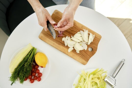 Top view of female hands peeling garlic and preparing ingredients for a fresh salad in a bright kitchen
