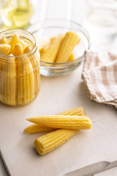 Fresh Baby Corn Cobs On Kitchen Counter With Jarred Preserved Vegetables For Cooking