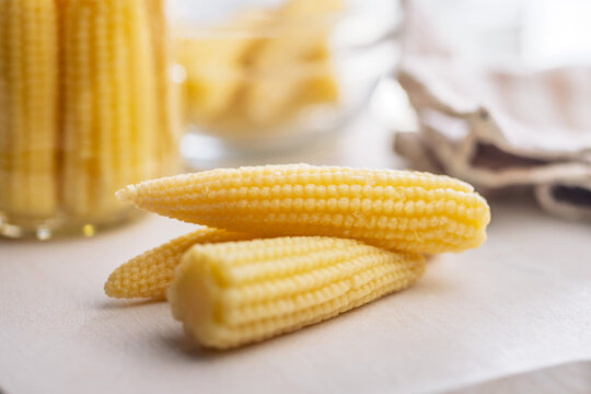 Fresh Baby Corn Cobs On Kitchen Counter With Jarred Preserved Vegetables For Cooking