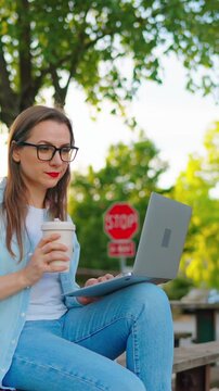 Woman sitting in the park with laptop after work day in the office. Slow motion