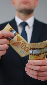 Formally dressed man carelessly throws Canadian Dollar bills towards the camera