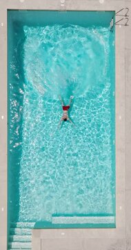 Aerial view as a man dives into the pool and swims. Slow motion