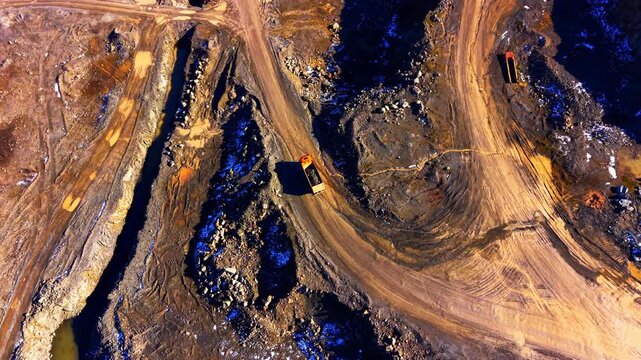Top down view of dump truck on quarry road, Bulgaria. Vehicle winding past blue tinted rock and muddy tracks in open pit.