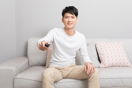 Young man holding remote control while watching television on sofa at home