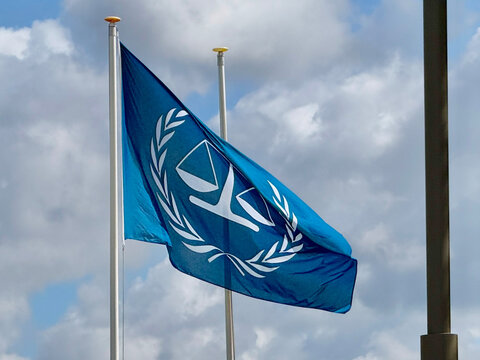 The Hague, Netherlands - June 11 2026: A blue flag with the International Criminal Court emblem waves on a flagpole. White clouds are visible in the bright blue sky.