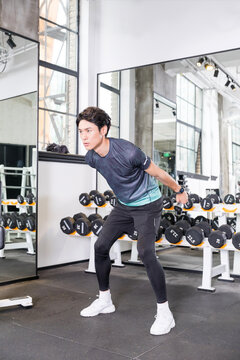Young man performing bent-over dumbbell reverse fly in modern gym