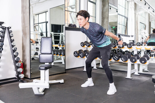 Young man doing dumbbell tricep kickbacks in modern gym