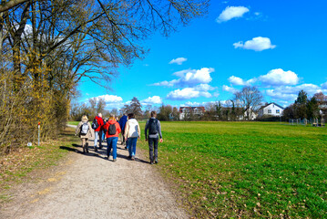 Obraz premium Gruppe von Wanderern mit Rucksäcken auf einem Spazierweg an einer großen Wiese im Frühling in Kahl am Main, Bayern