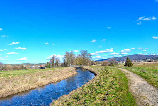 Feldweg entlang des Flusses Kahl mit hohen Pappeln und Blick auf den Vorspessart im Fr&uuml;hling in Kahl am Main, Bayern