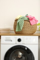 Crumpled clothes in laundry basket and washing machine indoors