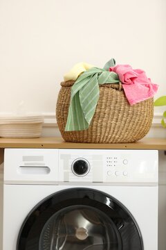 Crumpled clothes in laundry basket and washing machine indoors