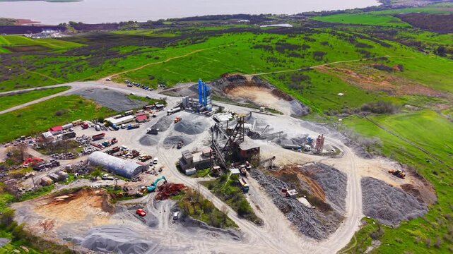 Quarry processing plant near lake. Elevated angle reveals silos, storage tower, gravel piles and surrounding green farmland.