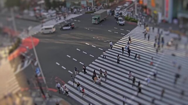 High angle tilt shift timelapse of a large city intersection in Tokyo with vehicles and pedestrians moving through a wide zebra crossing.